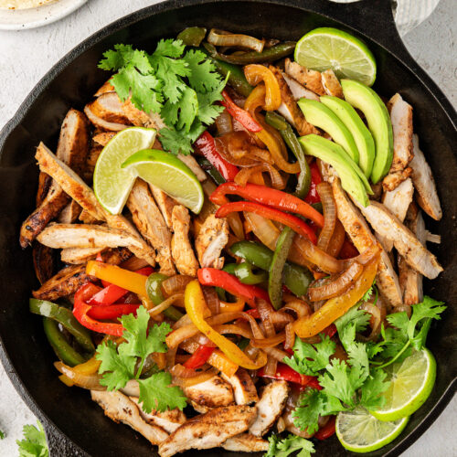 Chicken fajitas with peppers, lime wedges, and cilantro in cast iron skillet.