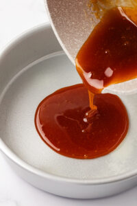 Pouring flan caramel sauce into cake pan.