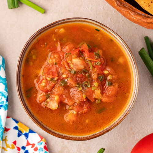 Ranchero sauce in bowl shown with tortilla chips and peppers on the side.