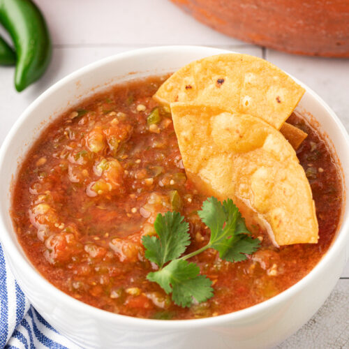 Red tomato-based salsa in a bowl with tortilla chips dipped into it.