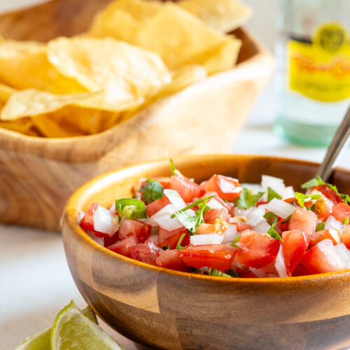 Bowl of pico de gallo shown with lime wedges and chips.