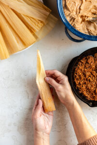 Folding a tamale after filling with masa and pork.