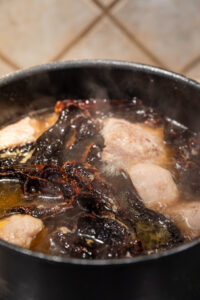 Boiling Boston butt pork roast with ancho chile peppers.