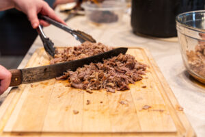Chopping cooked pork on a cutting board to make picadillo for tamales.